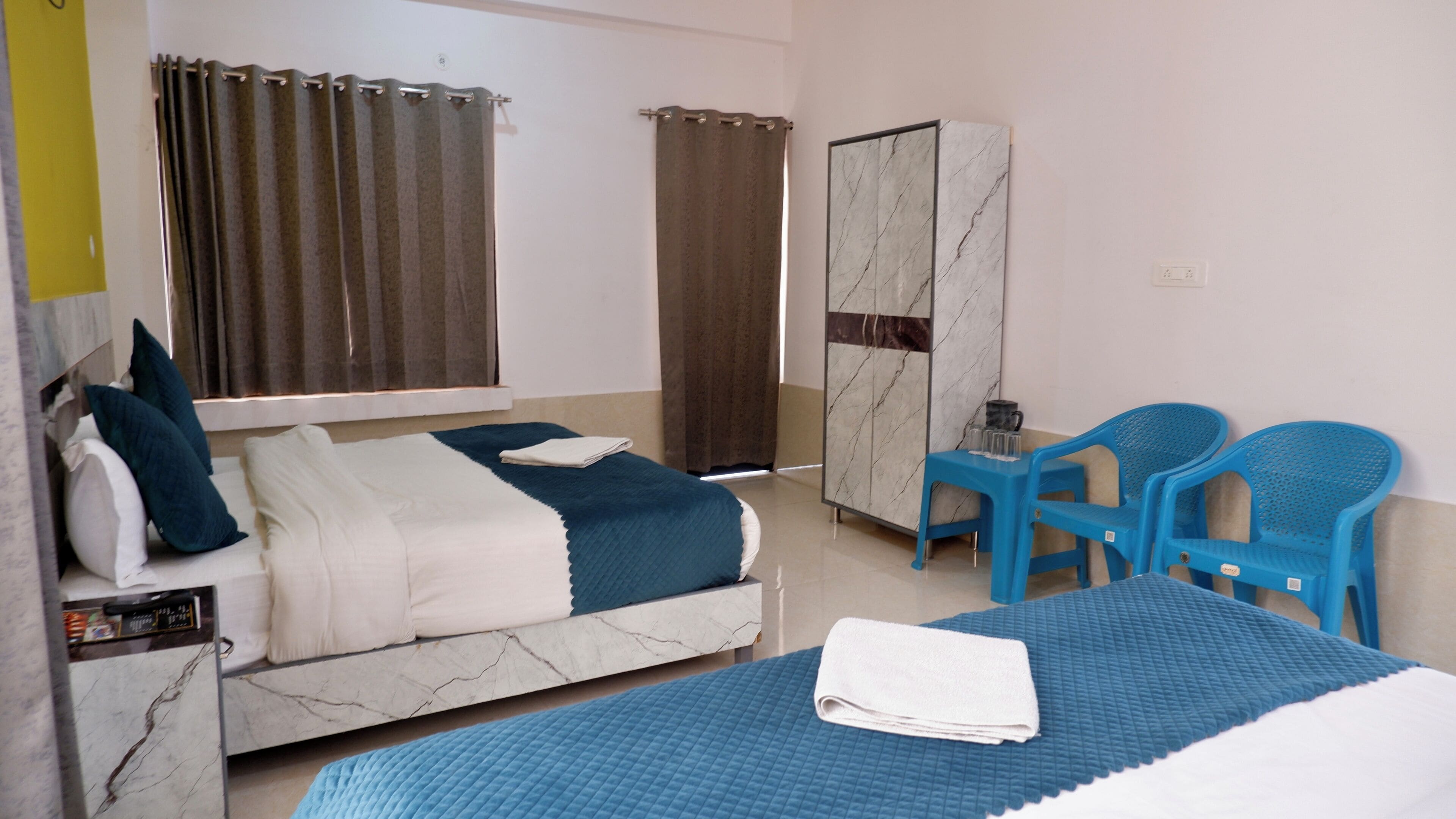 Ein Hotelzimmer mit einem Bett, einem Schreibtisch, zwei Stühlen, einem Kleiderschrank und Vorhängen.