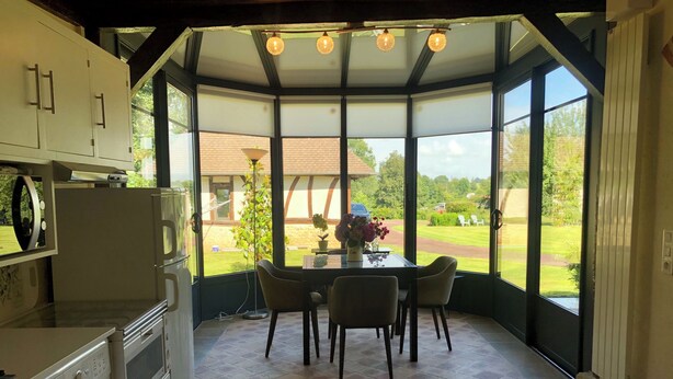 A kitchen with a washing machine, a dining table with chairs, and a view of a garden through large windows. - Renovated bread oven in pretty Normandy property (Étréville)
