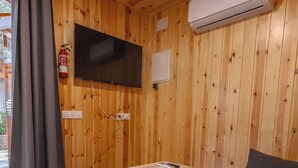 Una habitación con paneles de madera, un sofá, una mesa, un televisor de pantalla plana en la pared y un equipo de aire acondicionado.