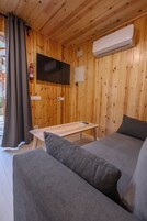 Una habitación con paneles de madera, un sofá, una mesa, un televisor de pantalla plana en la pared y un equipo de aire acondicionado.