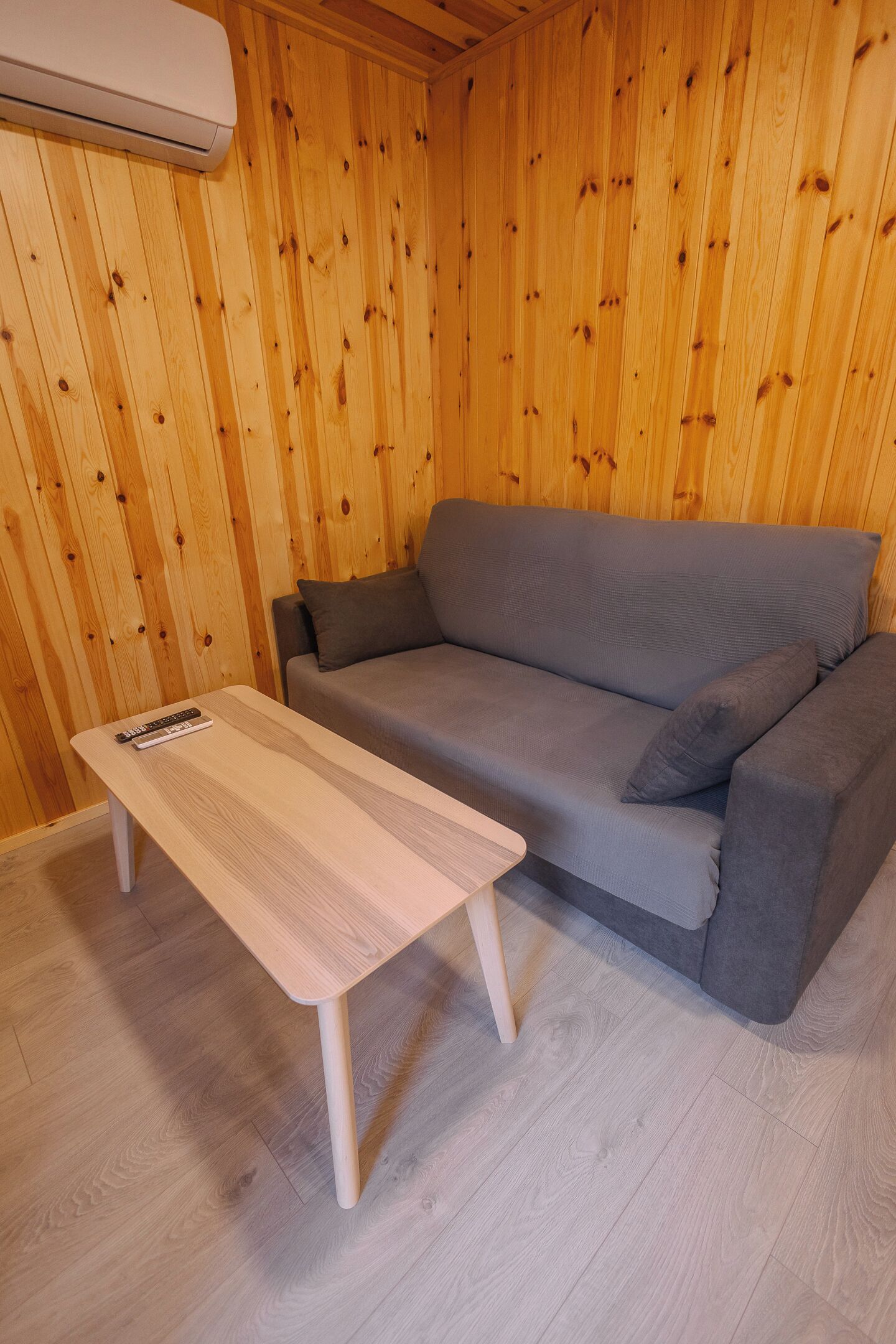 A wooden-paneled room with a grey sofa and a small white table.