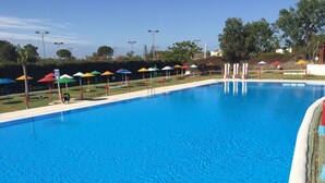 Una piscina con barandilla roja de seguridad, rodeada de sombrillas de colores y una zona ajardinada.