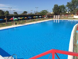 Una piscina con barandilla roja de seguridad, rodeada de sombrillas de colores y una zona ajardinada.