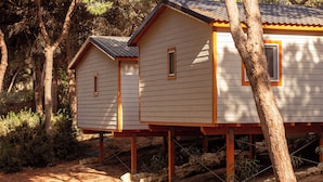 Dos cabañas de madera con techo inclinado, elevadas sobre pilotes, rodeadas de árboles y maleza.