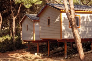 Dos cabañas de madera con techo inclinado, elevadas sobre pilotes, rodeadas de árboles y maleza.