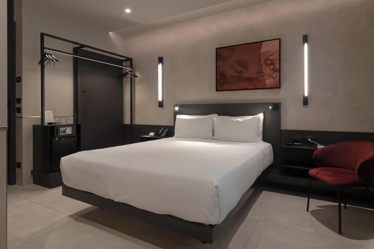 A modern hotel room with a large bed, a desk, a chair, and a shower area.