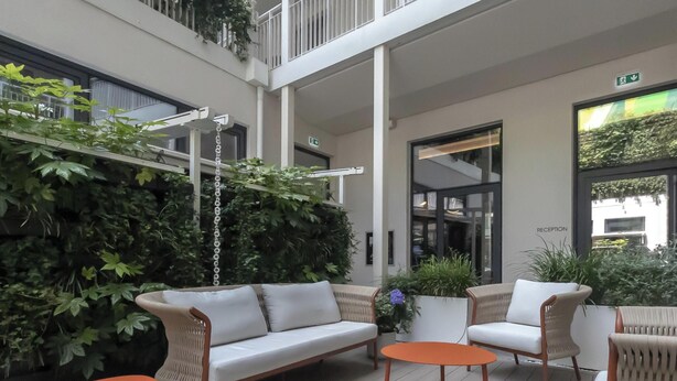 Un espacio exterior moderno con un sofá blanco, dos sillones y una mesita naranja.