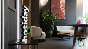 A modern hotel lobby with a reception desk, a sofa, a coffee table, and a large potted plant. - HOTIDAY Room Collection - Milano Cinque Giornate (Milan)