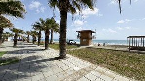 Ein Uferweg gesäumt von Palmen, mit einem Rettungsturm und einem Strand, auf dem eine hölzerne Bank steht.