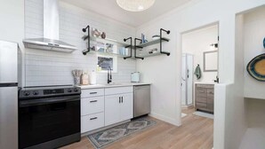A modern kitchen with white cabinetry, a stainless steel range hood, and black appliances. There are open shelves with kitchen items and a patterned rug on the floor.