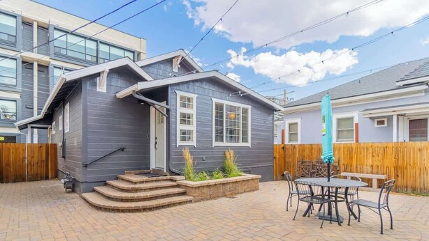 A two-story house with a grey exterior, a front porch with steps, and a patio area with a table and chairs.