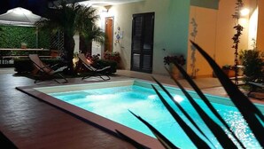 Un edificio di due piani con piscina, area salotto all'aperto e una zona coperta con piante.