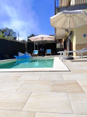 A swimming pool with lounge chairs and an umbrella, surrounded by a tiled patio.