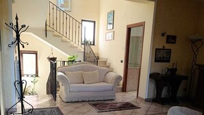 Un soggiorno con un divano, due tappeti, una scala e una porta che dà su un'altra stanza.
