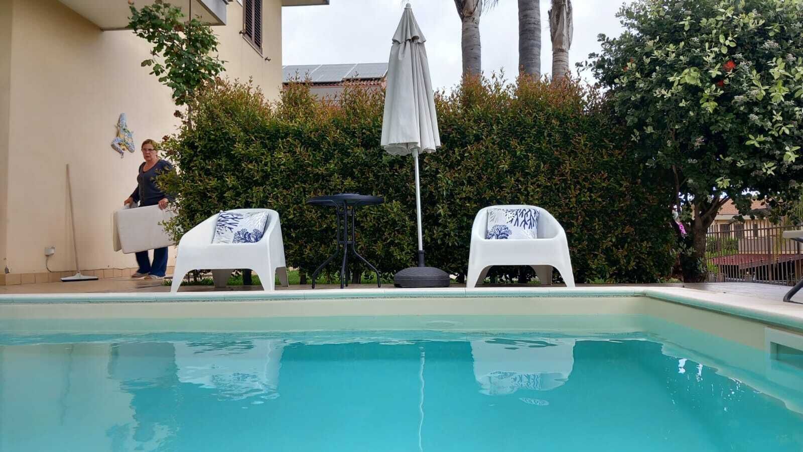Una piscina amb dues cadires blanques, una taula i una persona carregant una cadira.