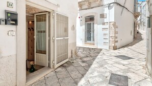 Una estrecha calle adoquinada con un edificio blanco que tiene una puerta de madera grande y un ventanal pequeño con barrotes.