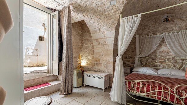 Un dormitorio con pared de piedra, cama con dosel, mesita de noche y ventana con cortinas.
