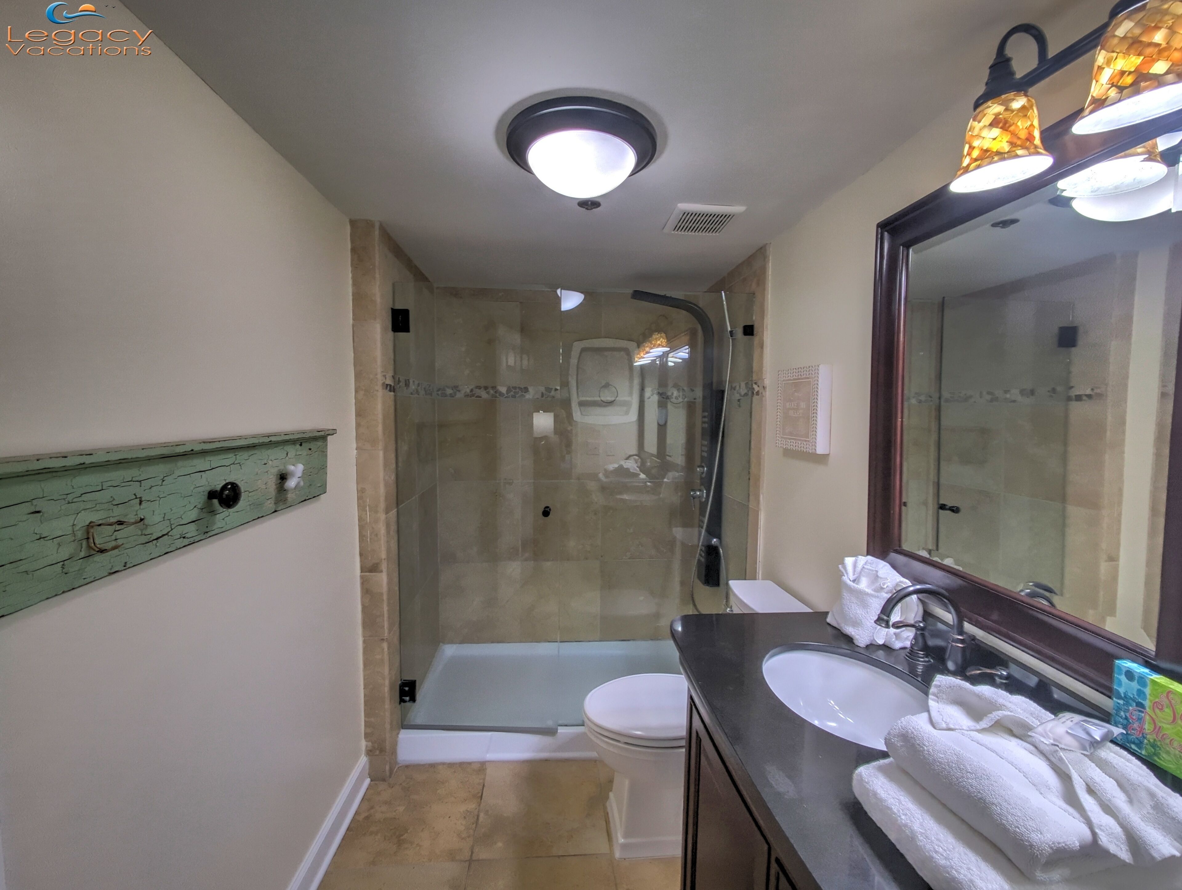 Une salle de bain avec une douche à parois de verre, des toilettes blanches, un lavabo avec un miroir et un porte-serviettes.