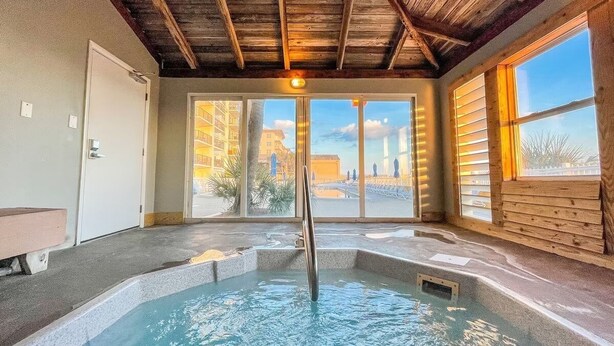 Un jacuzzi en una habitación con vigas de madera, ventanas amplias y vistas a edificios.