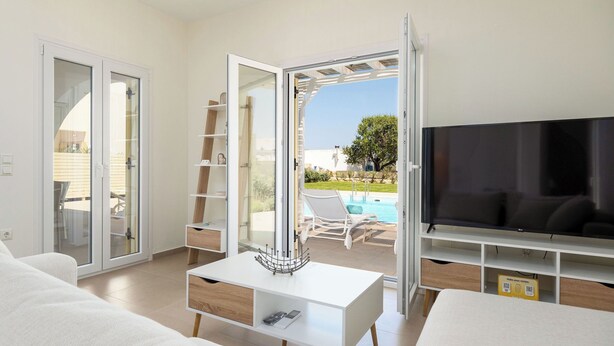 Un saló modern amb televisió, taula de centre i sofà. Hi ha una porta corredissa de vidre que dona a una zona de piscina.