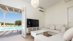 Un saló modern amb televisió, sofà i taula de centre, una porta de vidre que dona a una piscina, i un aparell d'aire condicionat.