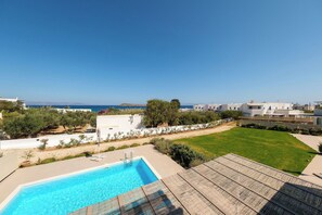 A swimming pool with a view of the sea, surrounded by greenery and white buildings.