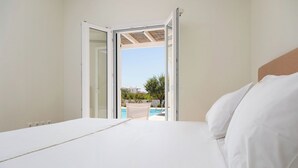Un dormitori amb un llit, una porta oberta que dona a un balcó amb vista a la piscina.