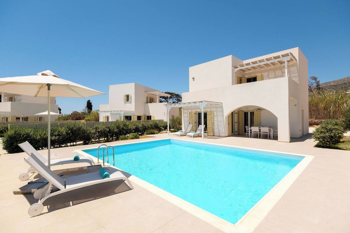 A modern pool area with lounge chairs and umbrellas, surrounded by a white building with a covered patio.