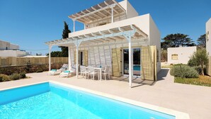 Una vila moderna amb piscina, mobiliari d'exterior i una pèrgola.