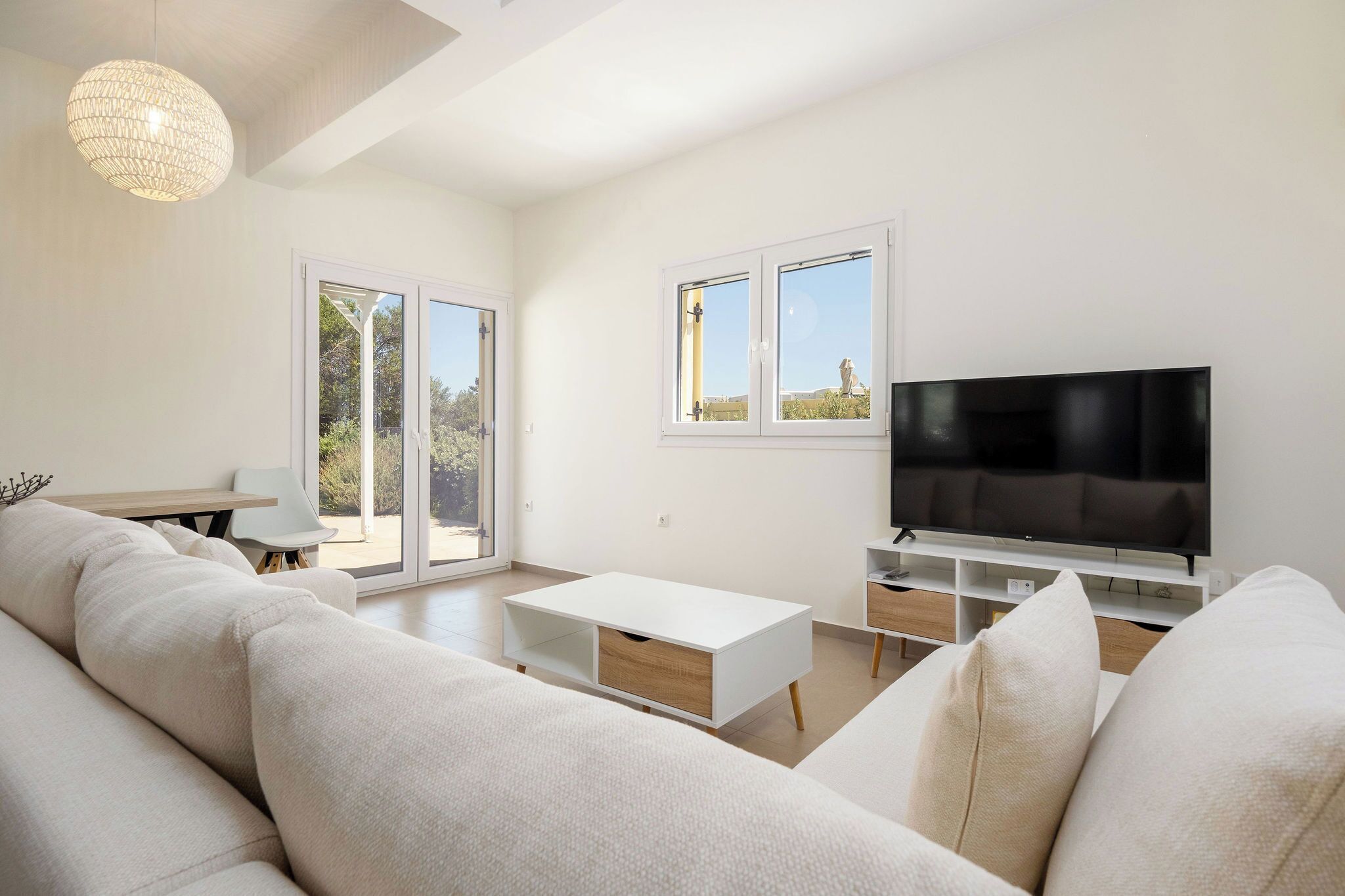 Una sala de estar moderna con un sofá blanco, un televisor y una zona de comedor con mesa y sillas.