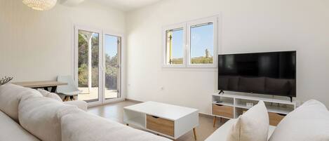 Una sala de estar moderna con un sofá blanco, un televisor y una zona de comedor con mesa y sillas.