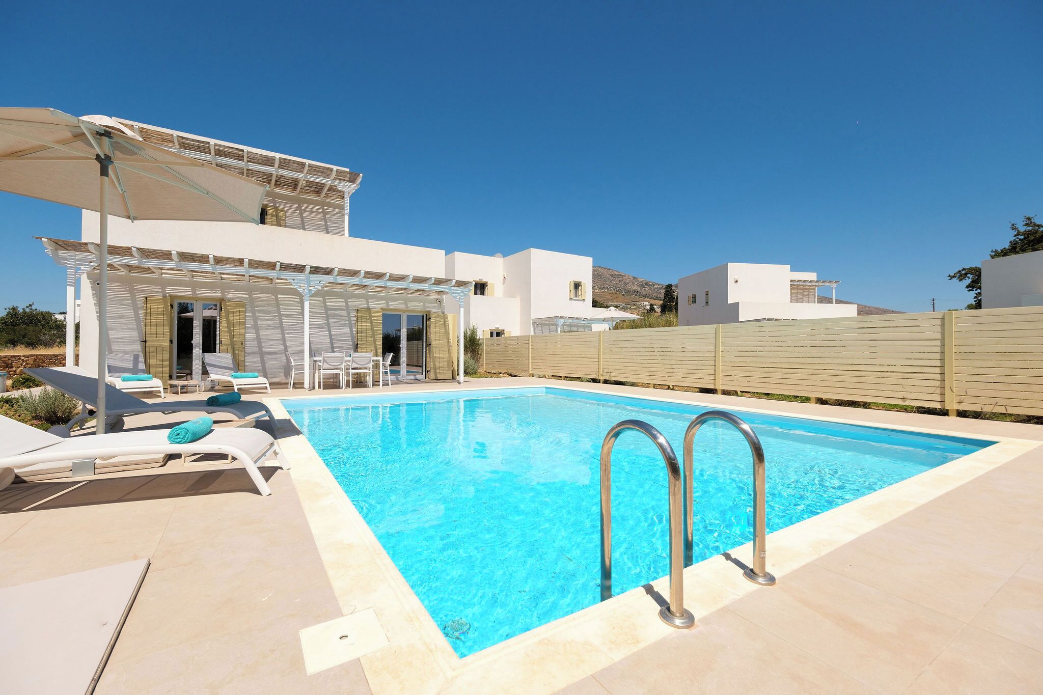 A modern pool area with a clear blue pool, sun loungers, and a covered seating area.