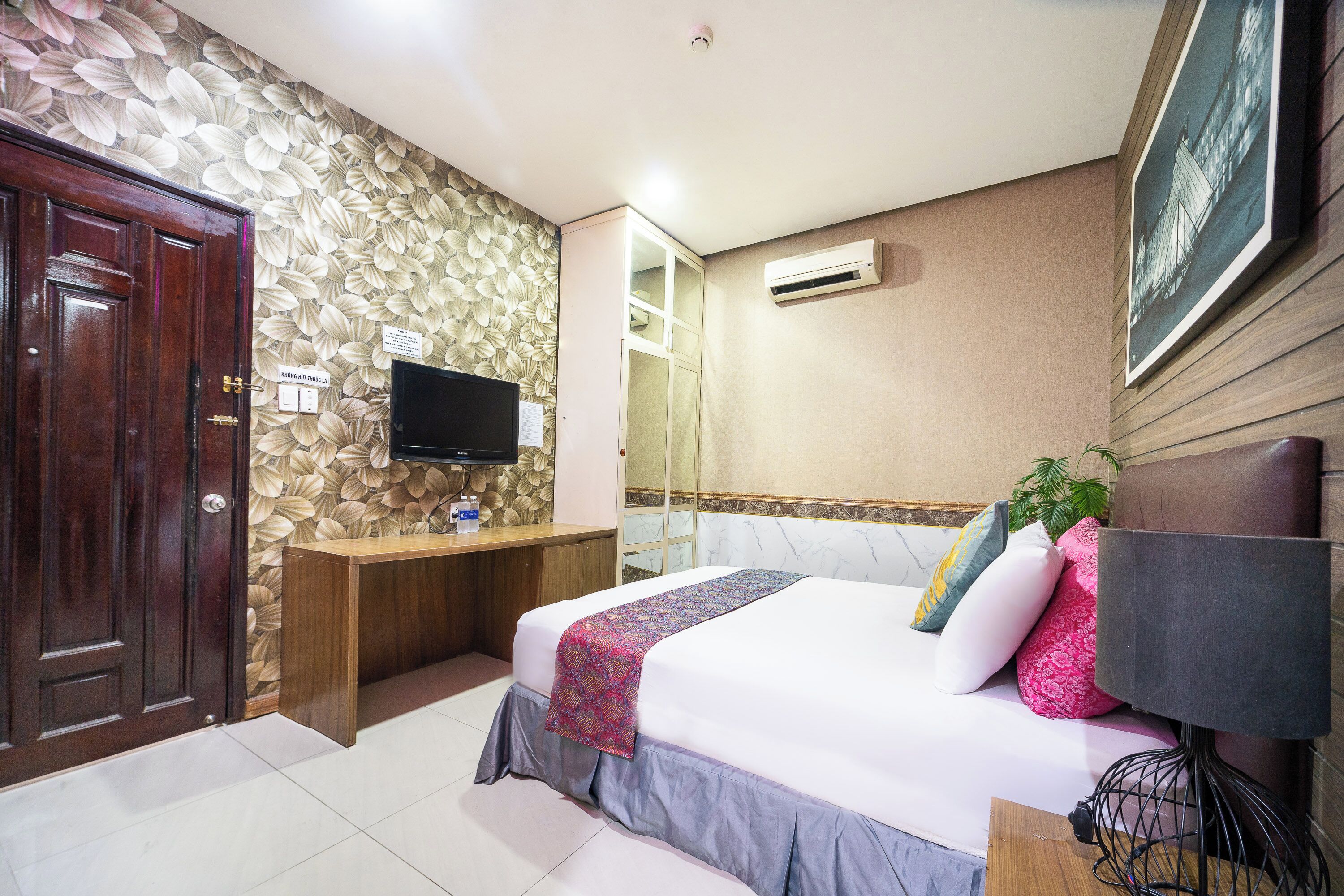 Une chambre d’hôtel avec un lit, une télévision, un bureau en bois et une armoire.