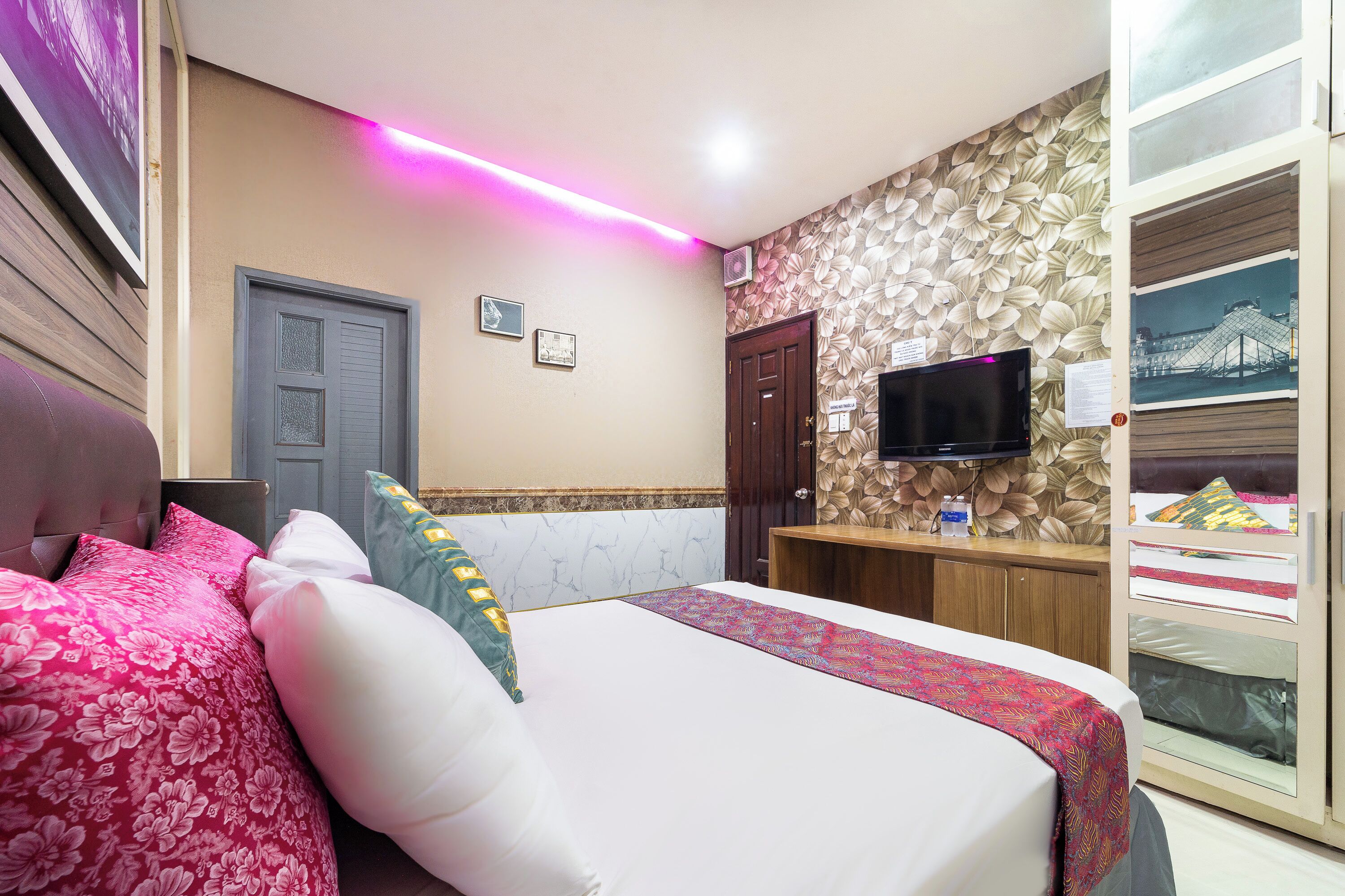 A hotel room with a bed, a desk, a television, and a wall with a leaf pattern.
