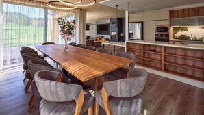 A modern kitchen with a wooden island, built-in appliances, and a large dining area with a wooden table and grey upholstered chairs. - Villa Albatros Paradise in the middle of Lauzitzer Gebirge and Golf Resort Malevil (Liberecký kraj)