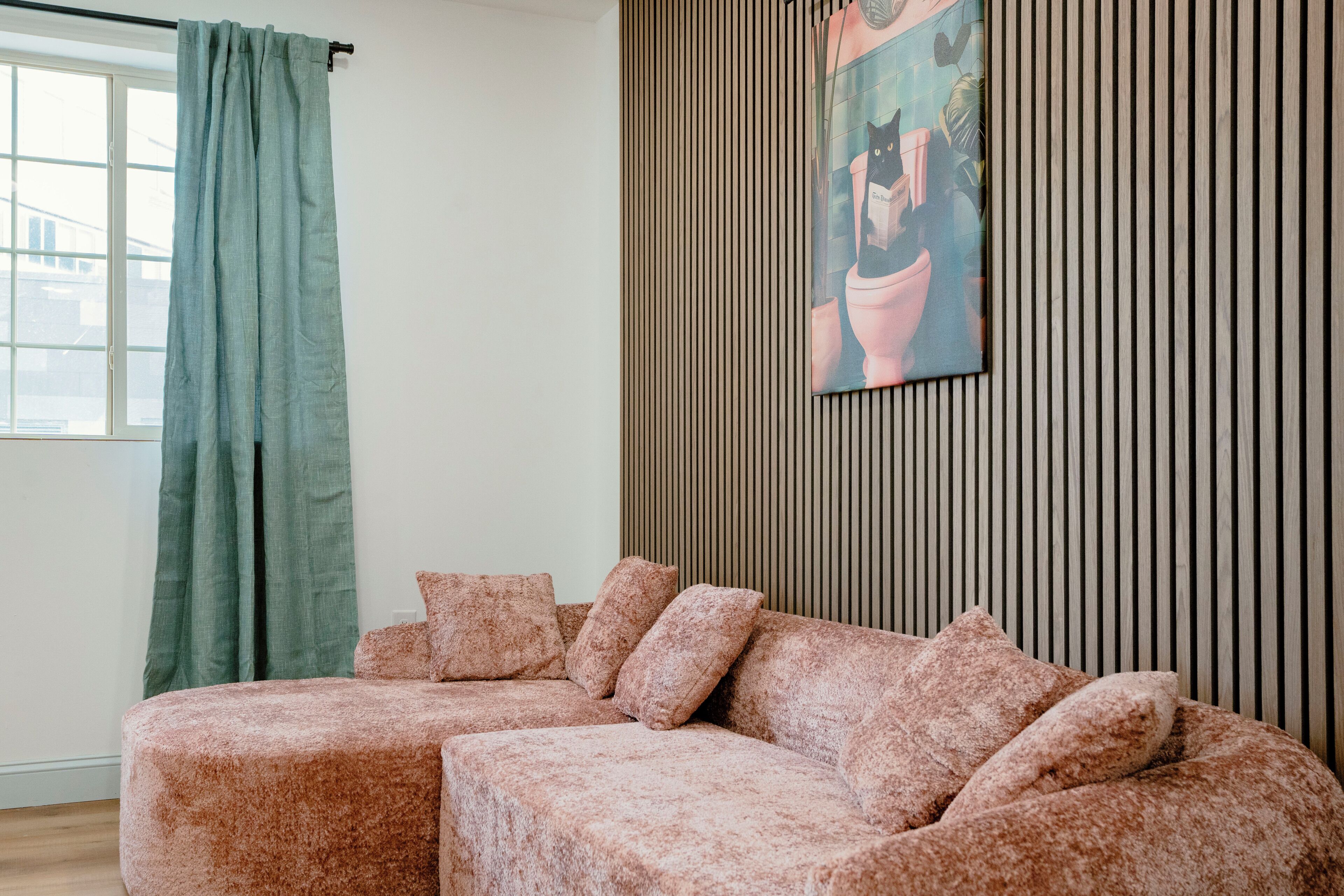 Una sala de estar con un sofá modular, una cortina verde y un panel de madera con un cuadro enmarcado.
