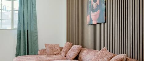 Una sala de estar con un sofá modular, una cortina verde y un panel de madera con un cuadro enmarcado.
