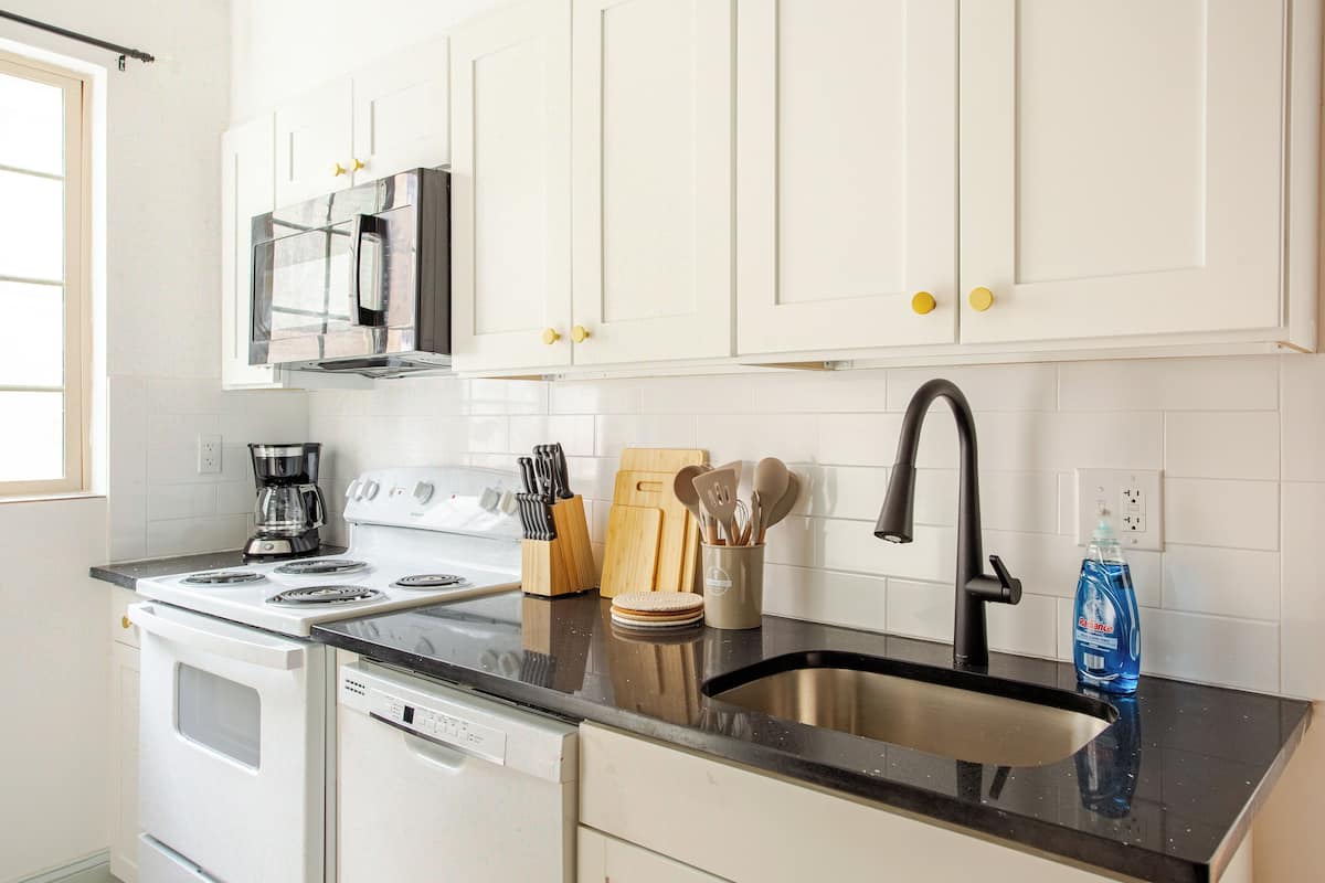 A kitchen with white cabinets, a black countertop, a stainless steel sink, a stove, and a dishwasher.