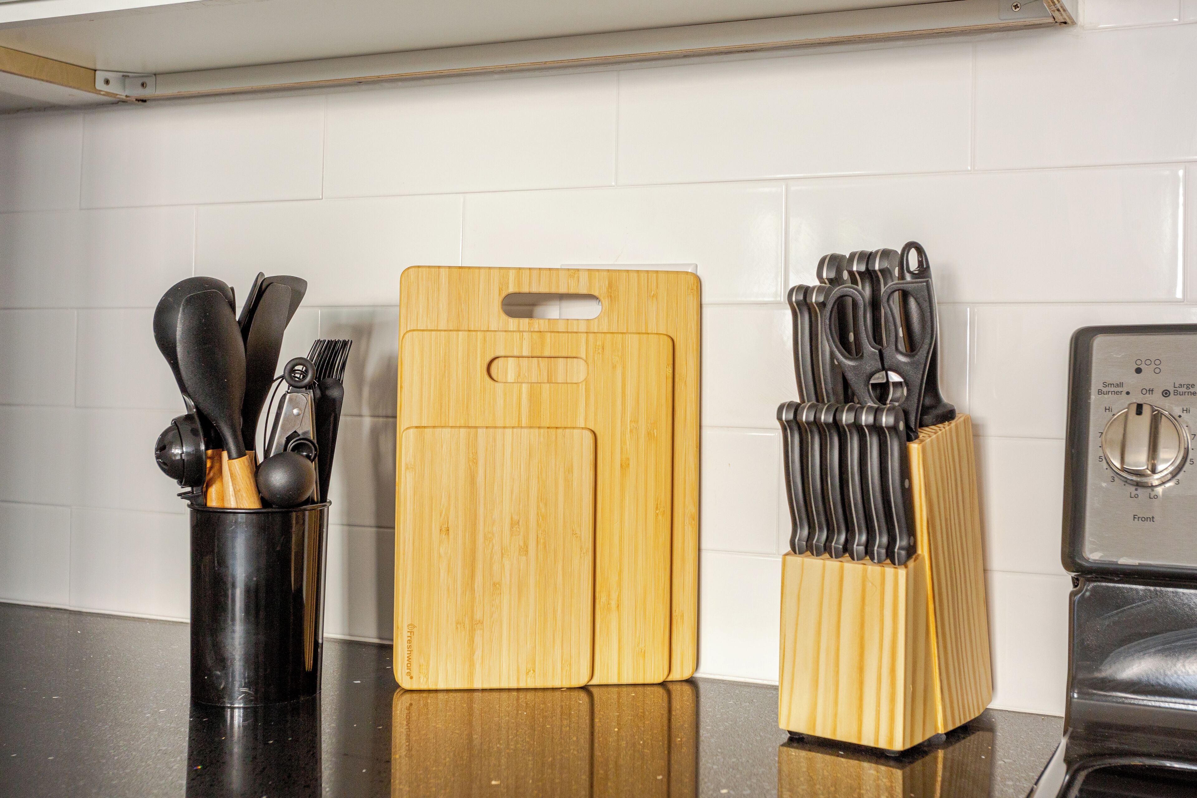A kitchen counter with a wooden cutting board, a utensil holder, and a toaster.
