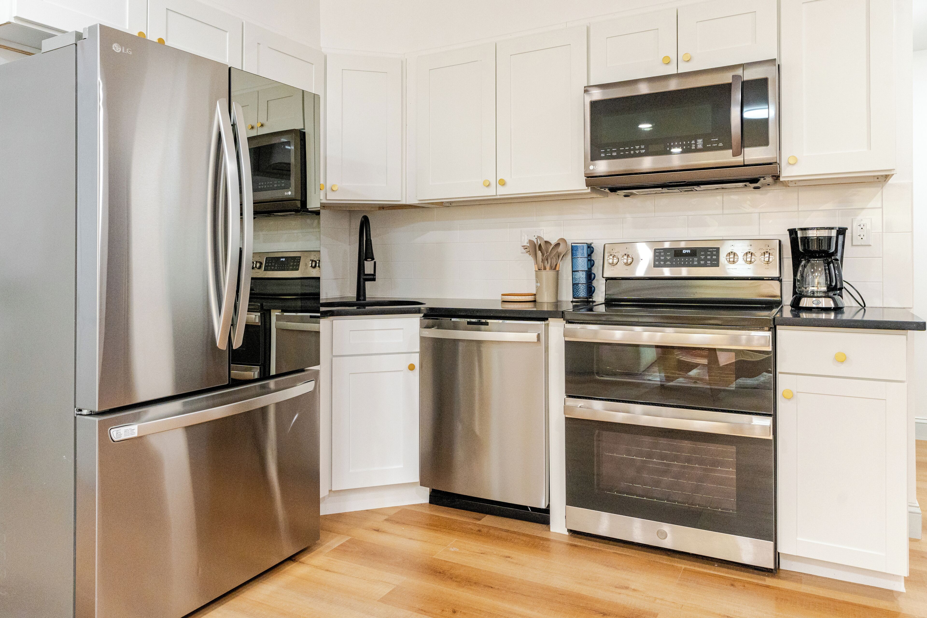 A modern kitchen with stainless steel appliances, white cabinetry, and a wooden floor.