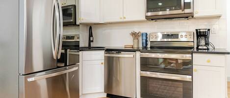 A modern kitchen with stainless steel appliances, white cabinetry, and a wooden floor.