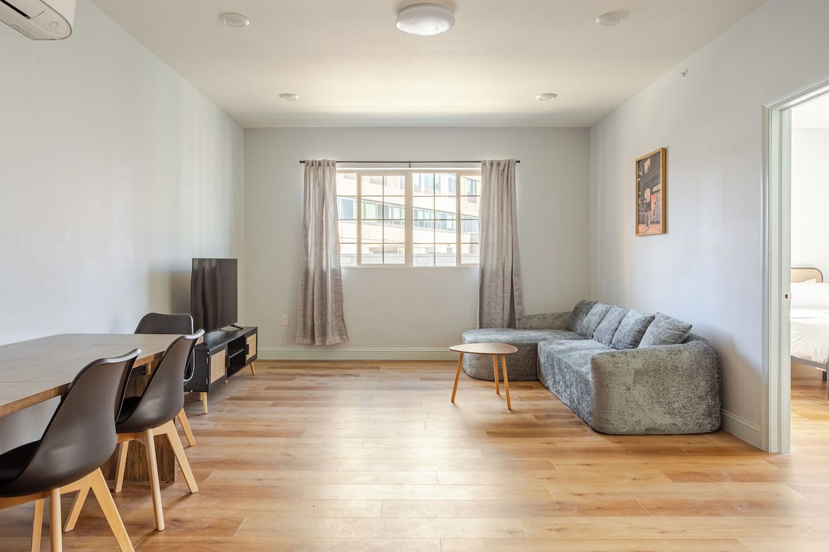 A modern living room with a wooden dining table, chairs, a grey sofa, and a small round table.