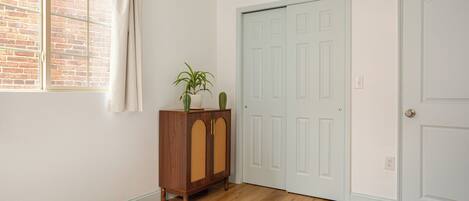 A room with a wooden floor, a white bed, a wooden cabinet with plants, and a white door with a window above it.