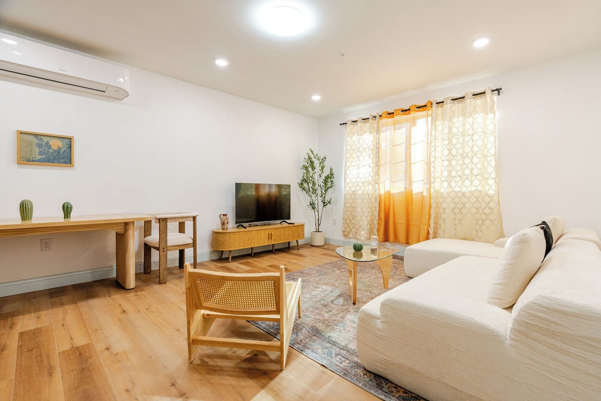 A modern living room with a sofa, a wooden dining table, a TV, and a plant.