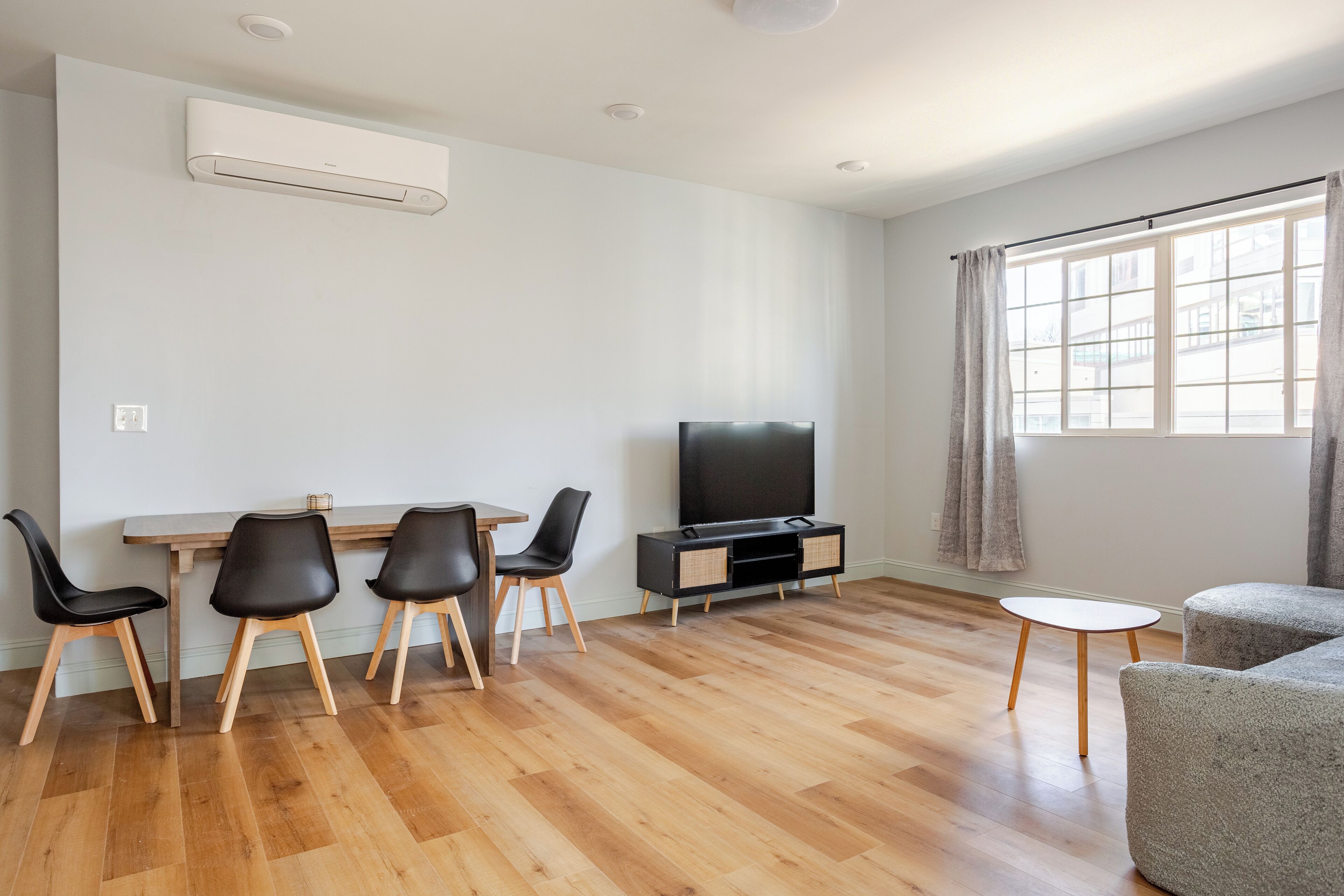 Een moderne woonkamer met houten vloer, een flatscreen televisie, een eettafel met stoelen en een bank.