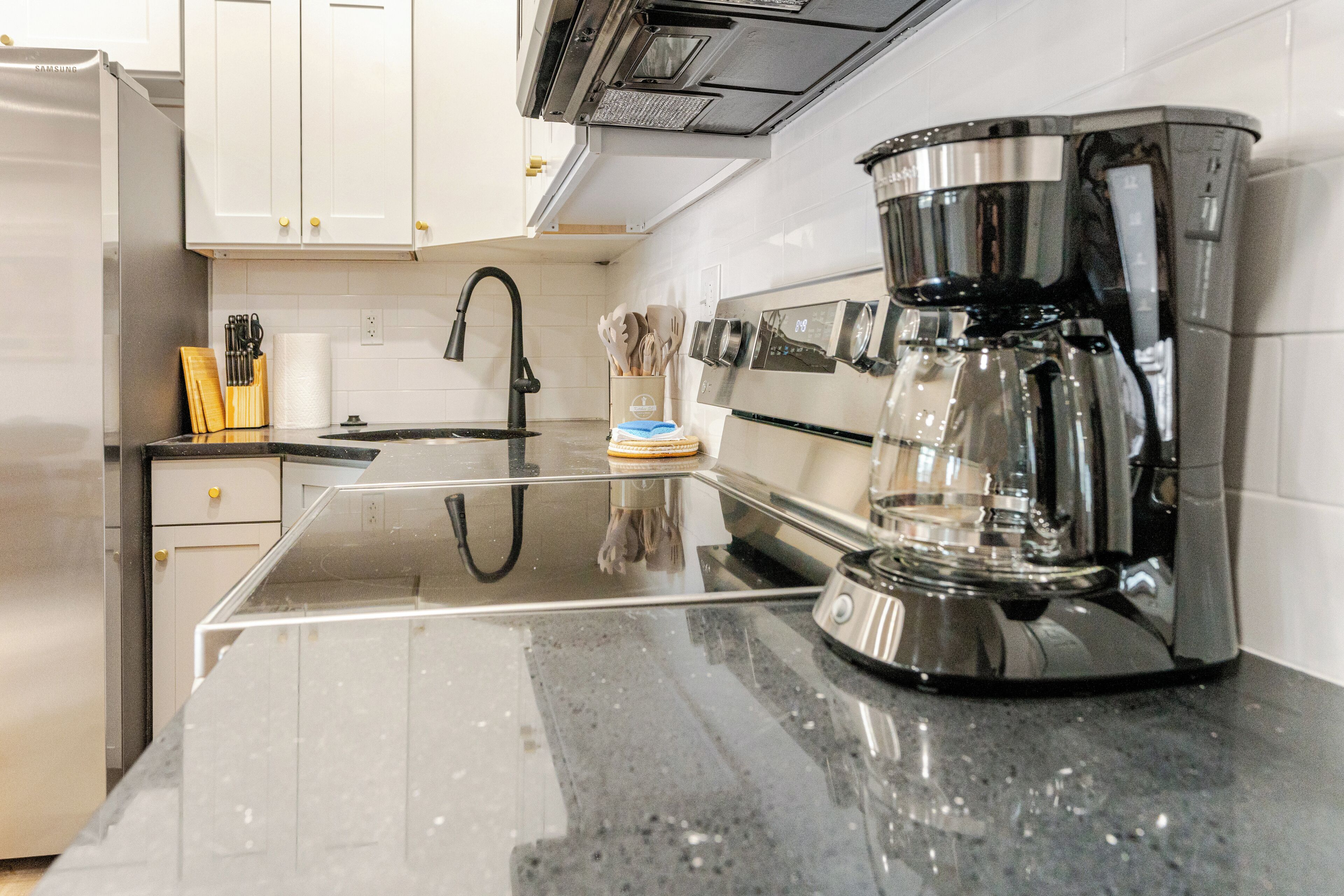 A modern kitchen with white cabinets, a stainless steel refrigerator, a black countertop, and a coffee maker.