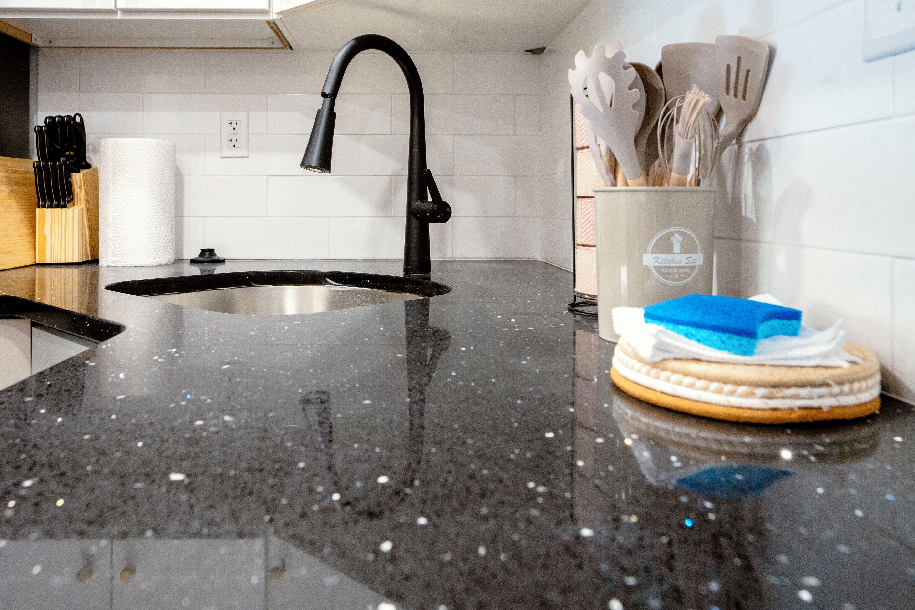 A kitchen with a black granite countertop, a stainless steel sink, and a paper towel holder.
