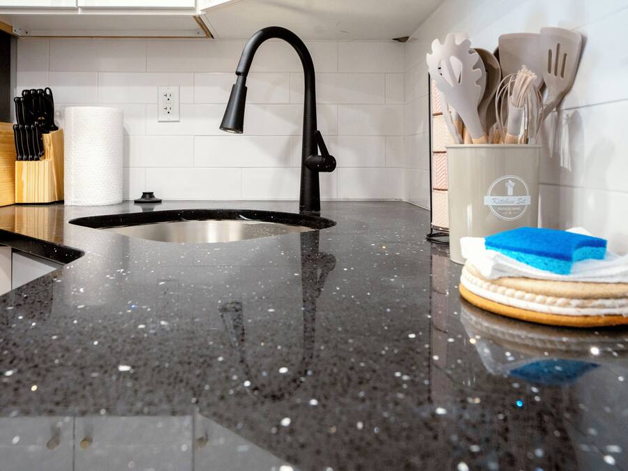 Una cocina con encimera de granito negro, pileta de acero inoxidable y dispensador de toallas de papel.