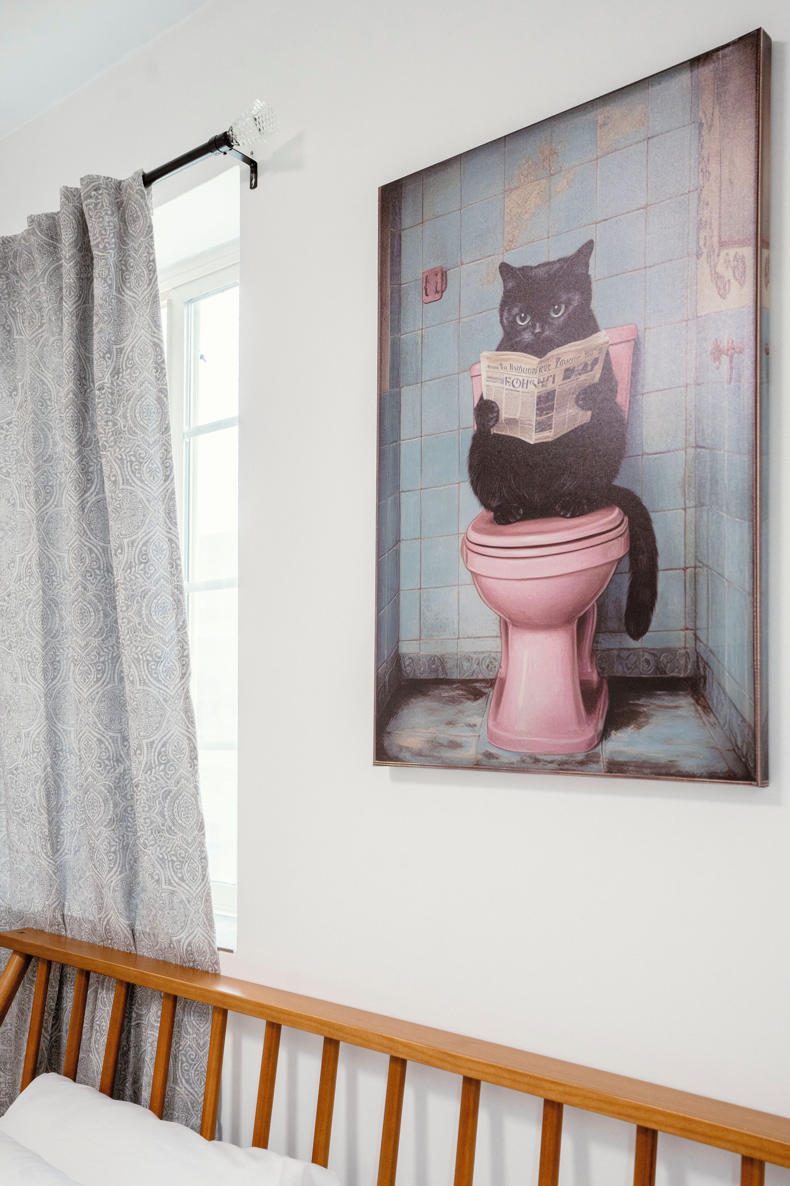 A bathroom with a pink toilet, a window with a curtain, and a painting of a cat on the toilet.