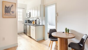 Een moderne keuken met witte kastjes, een roestvrijstalen koelkast en een koffiezetapparaat. Er is een eethoek met een ronde houten tafel en twee zwarte stoelen.